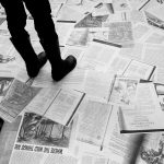 In black and white, papers strewn across the floor. Someone's feet are standing on them.